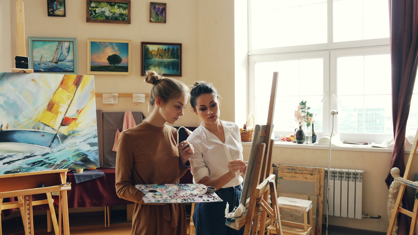 Umělec a student malují plachetnici v jasném ateliéru.